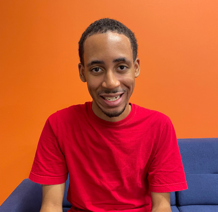 Man in red shirt smiling against orange background